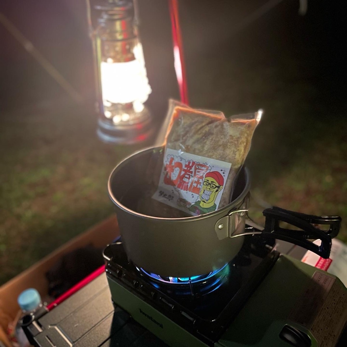 夜のキャンプ。ランタンの下で、バーナーのクッカーに真空パックを入れて湯せんしている
