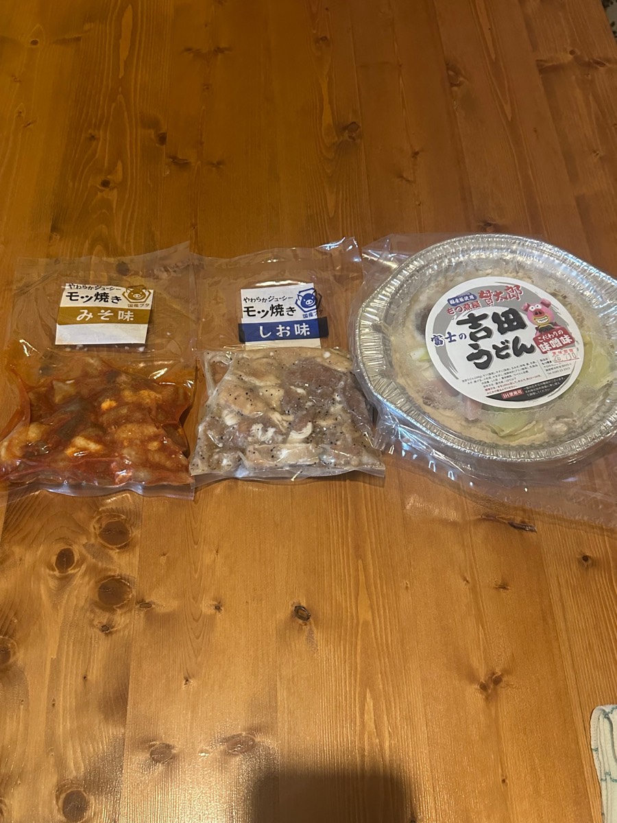 もつ焼き味噌・塩と〆うどんの真空パックを木の床に並べたキャンプ用のセット