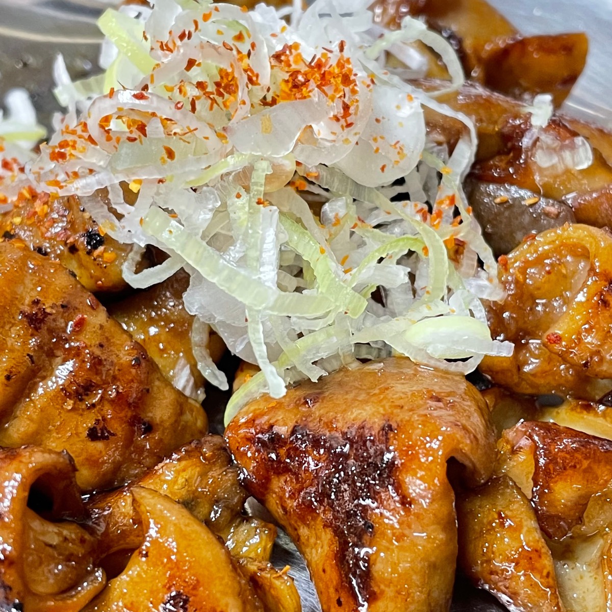 味噌だれの絡んだもつ焼きに、白髪ねぎと唐辛子をのせたところ
